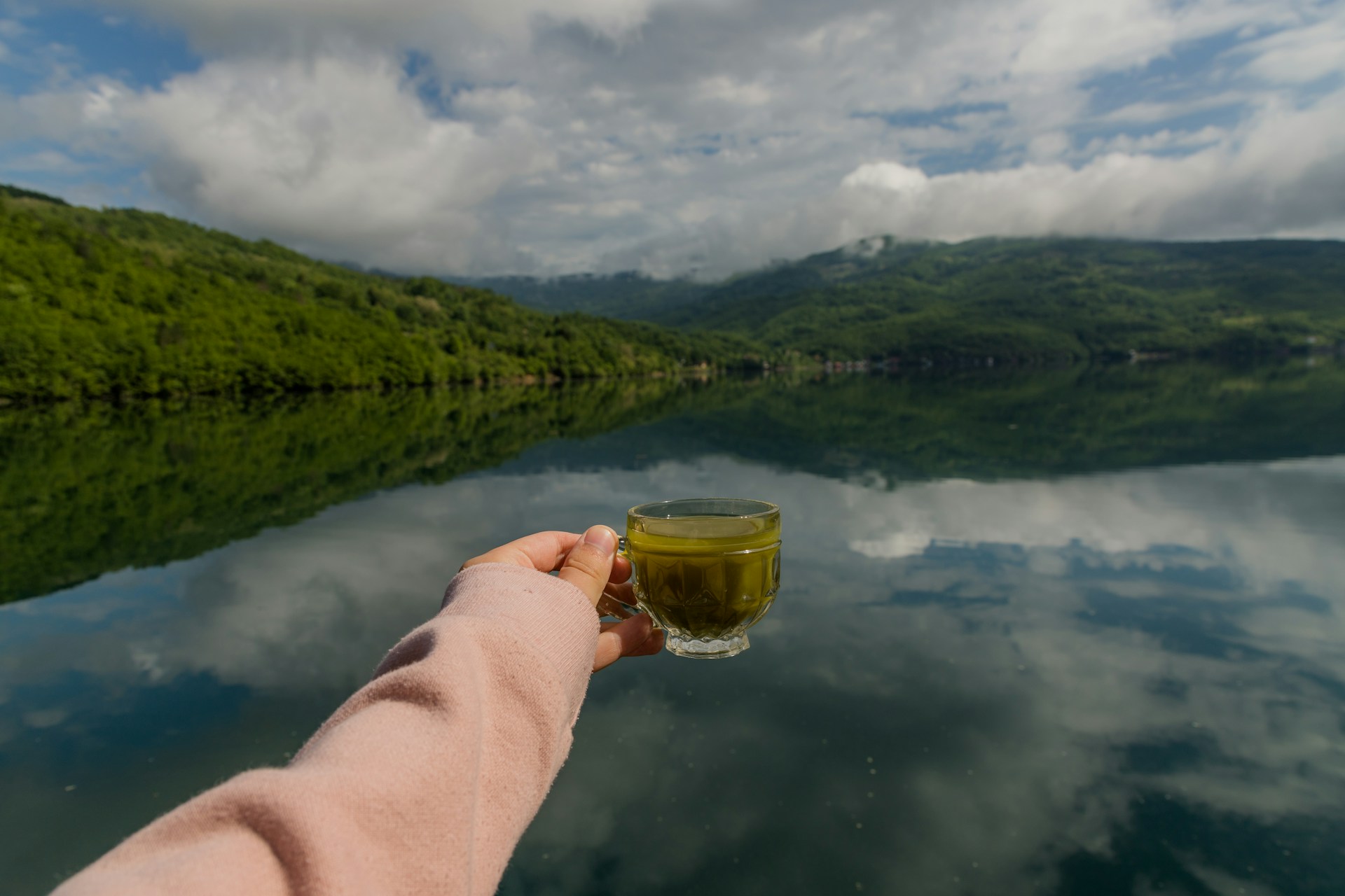 a person holding a cup of tea in front of a body of water