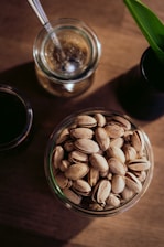a glass bowl filled with nuts next to a cup of coffee