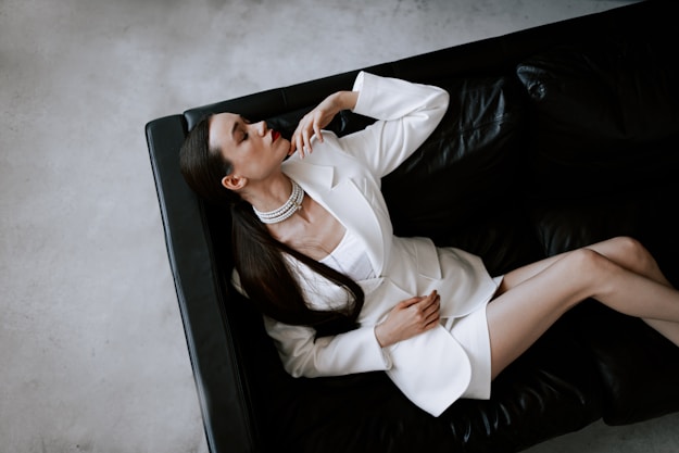 a woman in a white jacket and skirt sitting on a black couch