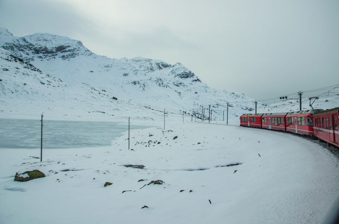 Red train passing snowy mountains in Europe