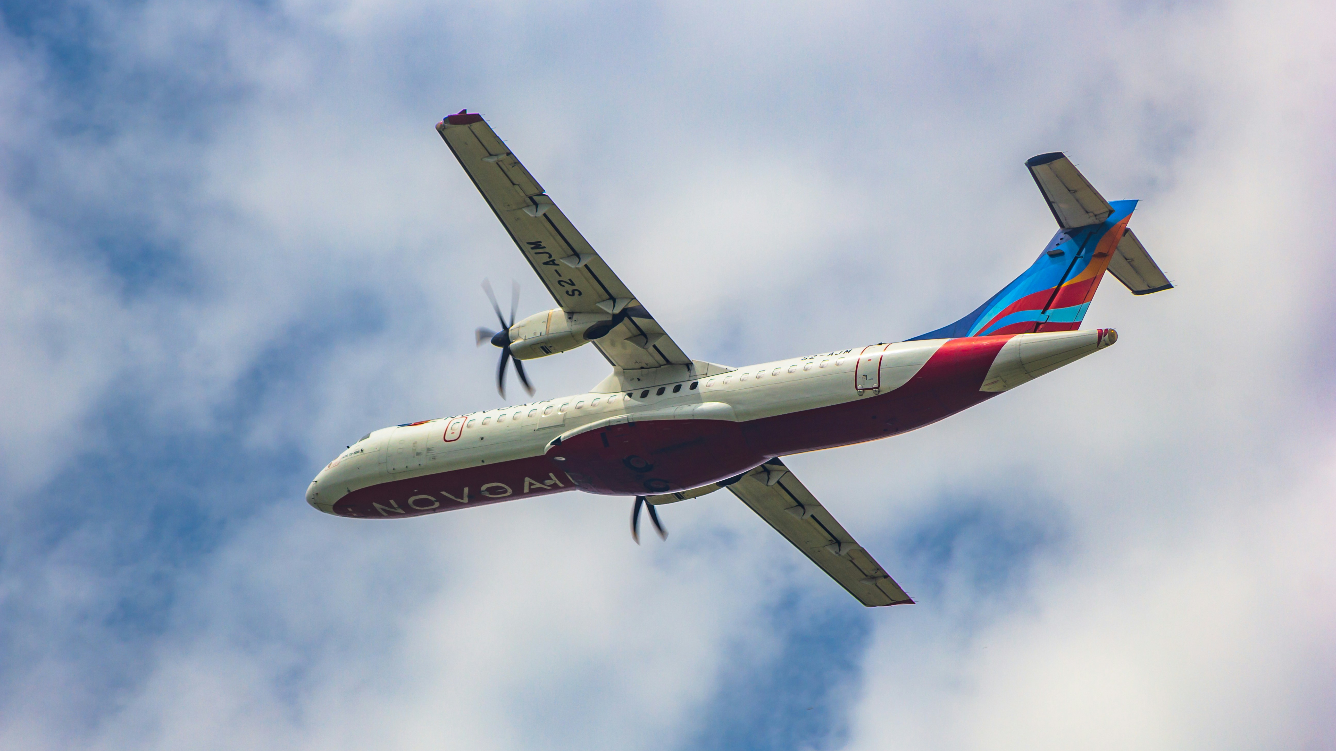 a large airplane flying through a cloudy blue sky, Novoair ATR 72-500