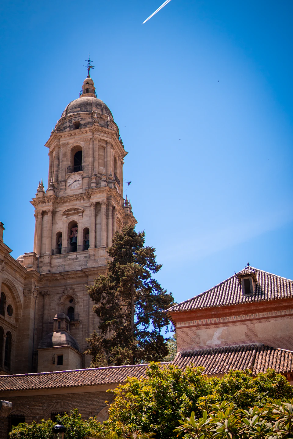 Tall stone church with clock tower stands against clear blue sky and lush greenery