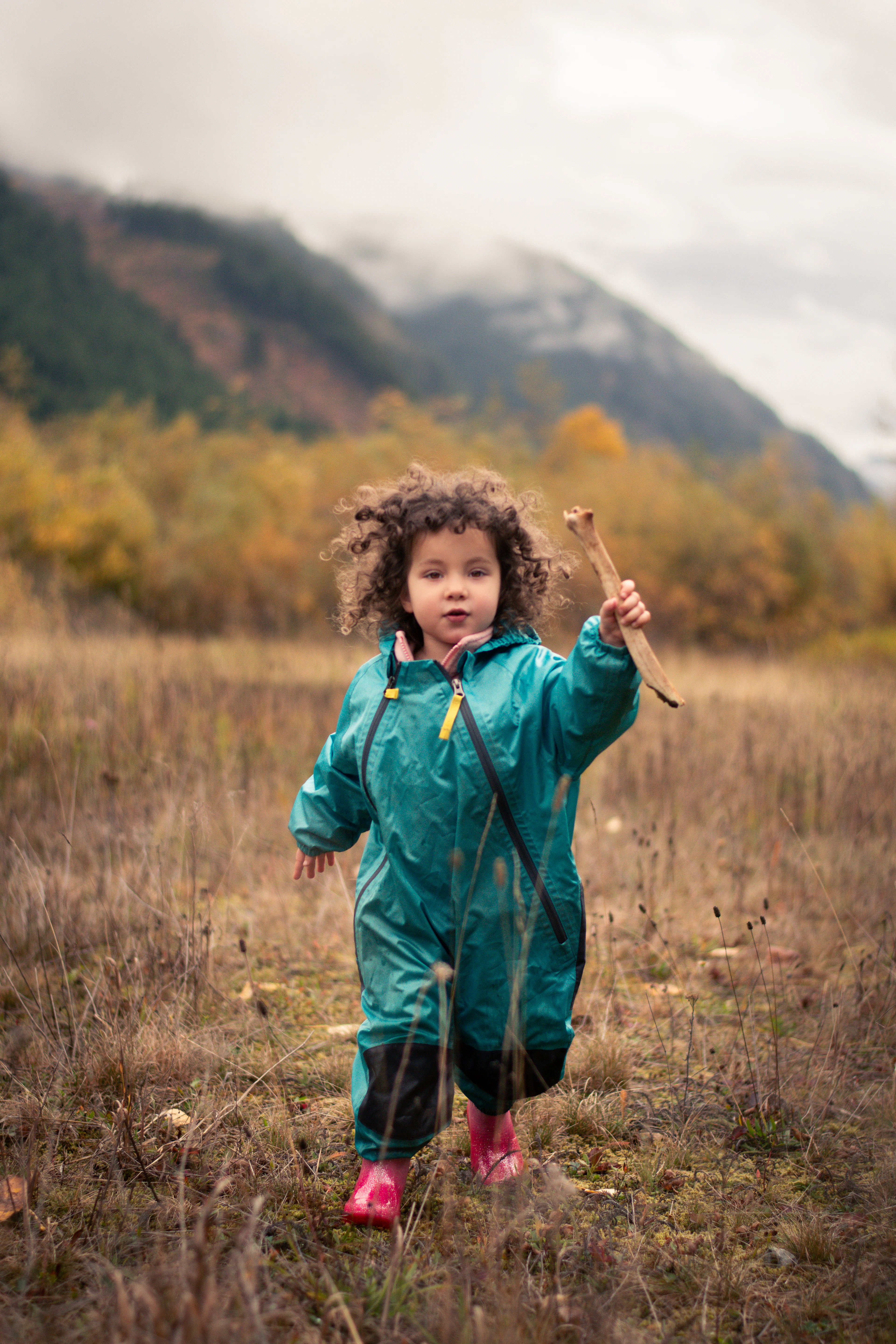 A toddler in a green rain suit holding a stick in a field