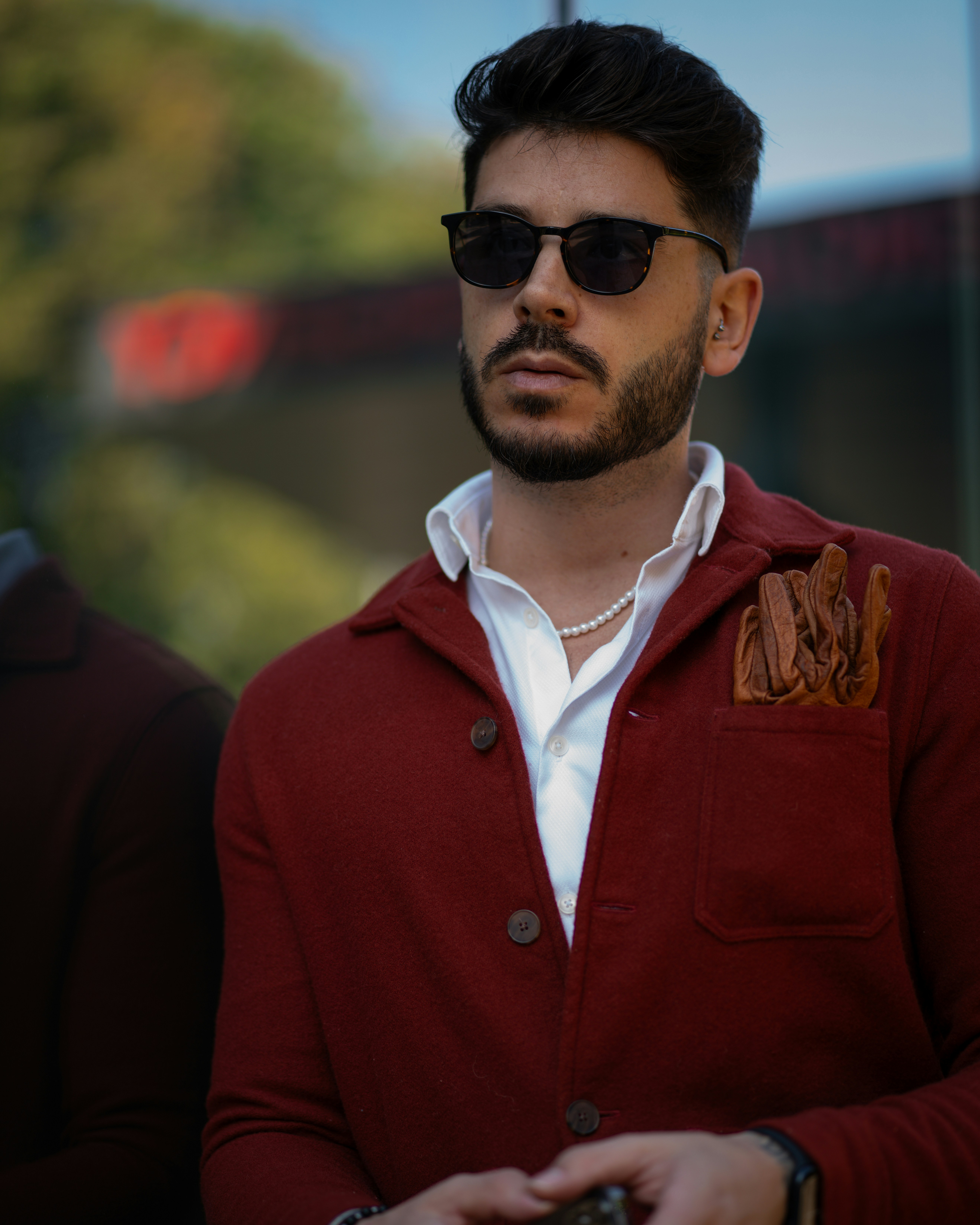 Radiating confidence, a bearded man dons a sharp red suit paired with sleek round acetate sunglasses, creating a chic and unforgettable look.