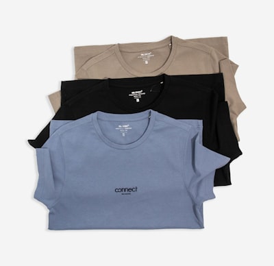 Folded cotton tees in tan, black and slate — photo by TuanAnh Blue on Unsplash