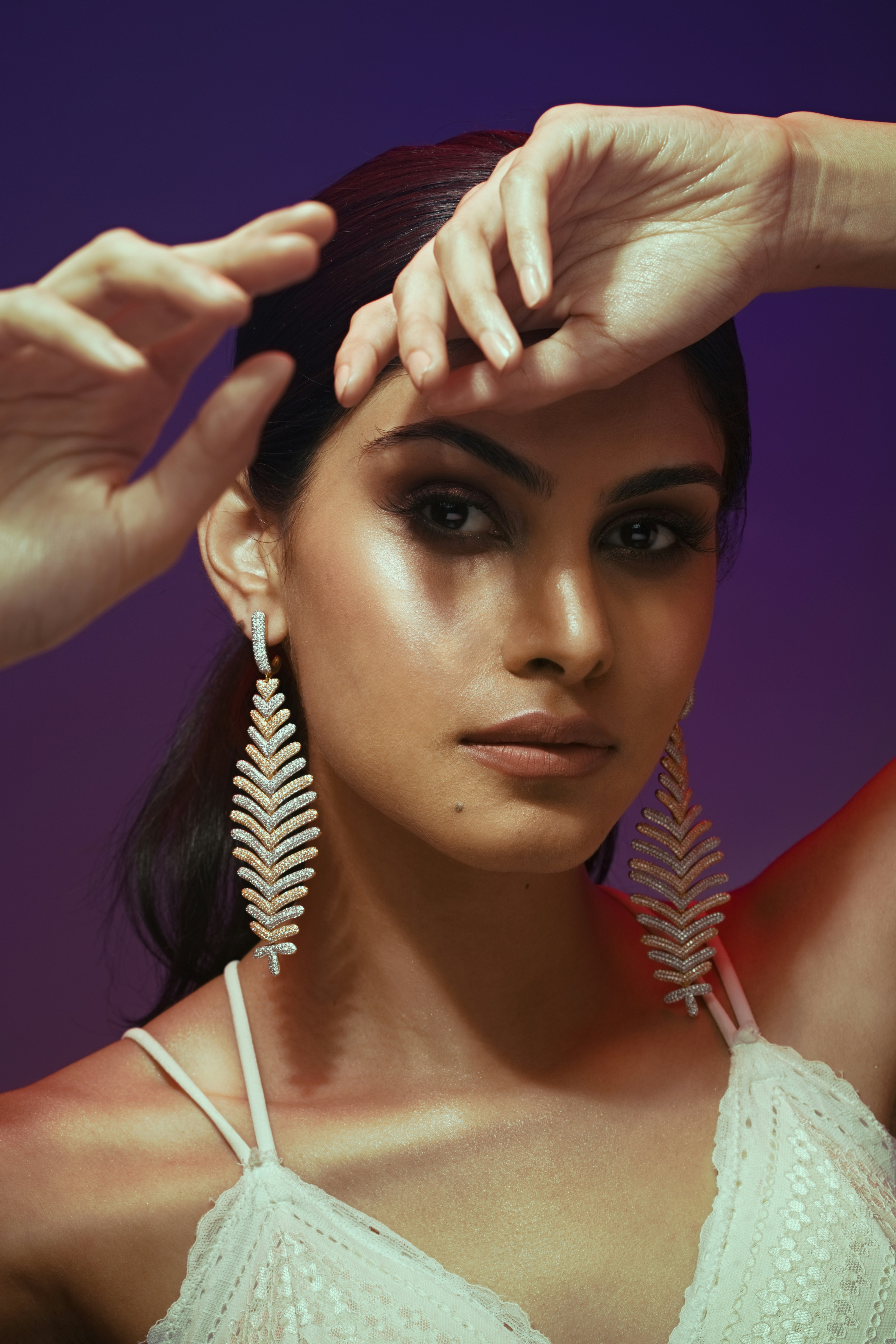 a woman in a white top is holding a pair of earrings