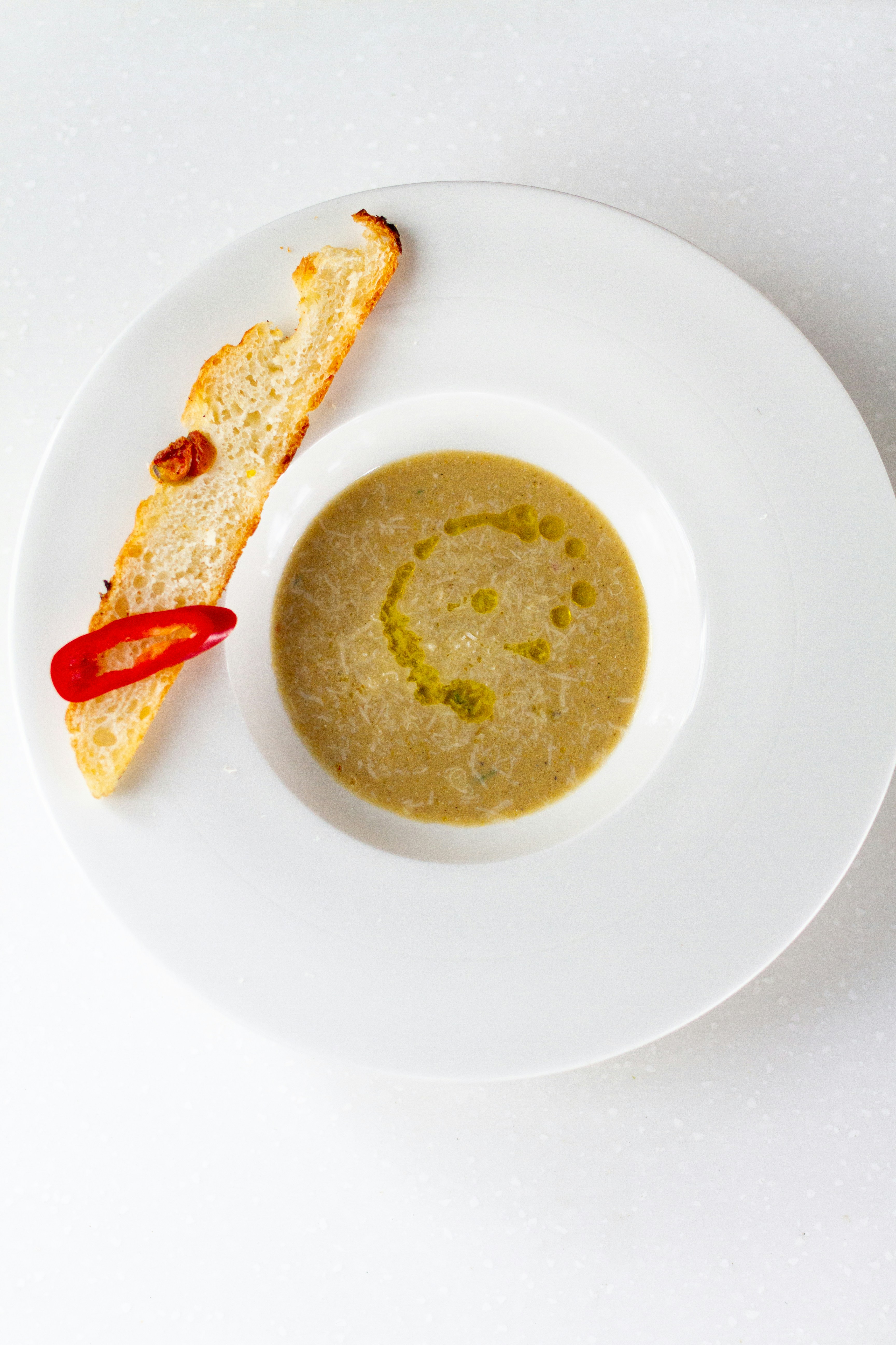 a white plate topped with a piece of bread and a bowl of soup