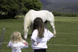 a woman and a little girl standing in front of a white horse