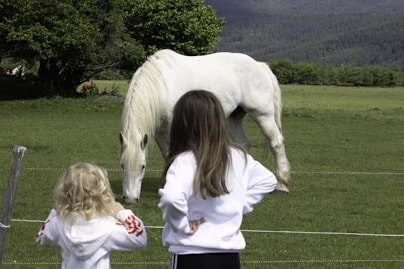 a woman and a little girl standing in front of a white horse