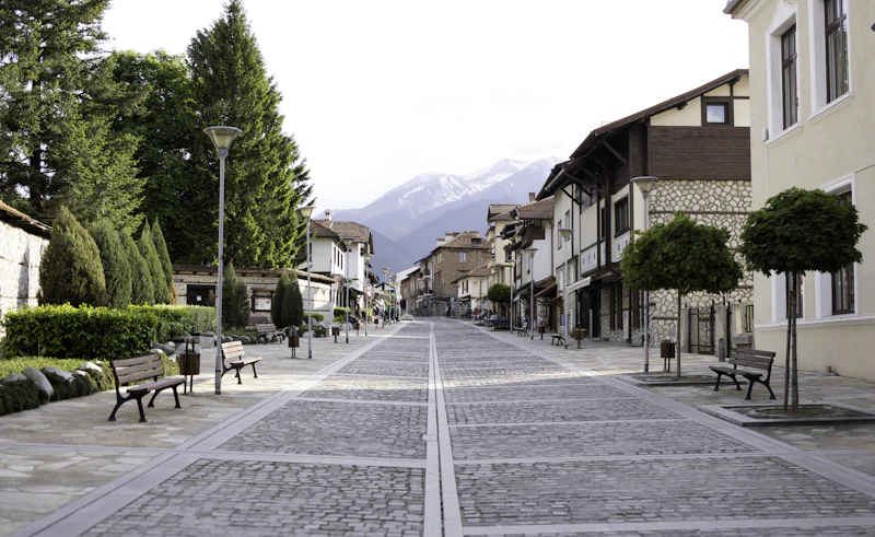 A cobbled street in the old centre of Bansko, lined with benches and trees.