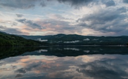 a body of water surrounded by mountains under a cloudy sky