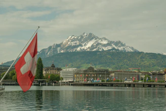a swiss flag is in the foreground of a lake with a mountain in the