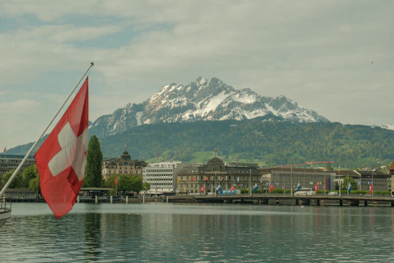 a swiss flag is in the foreground of a lake with a mountain in the