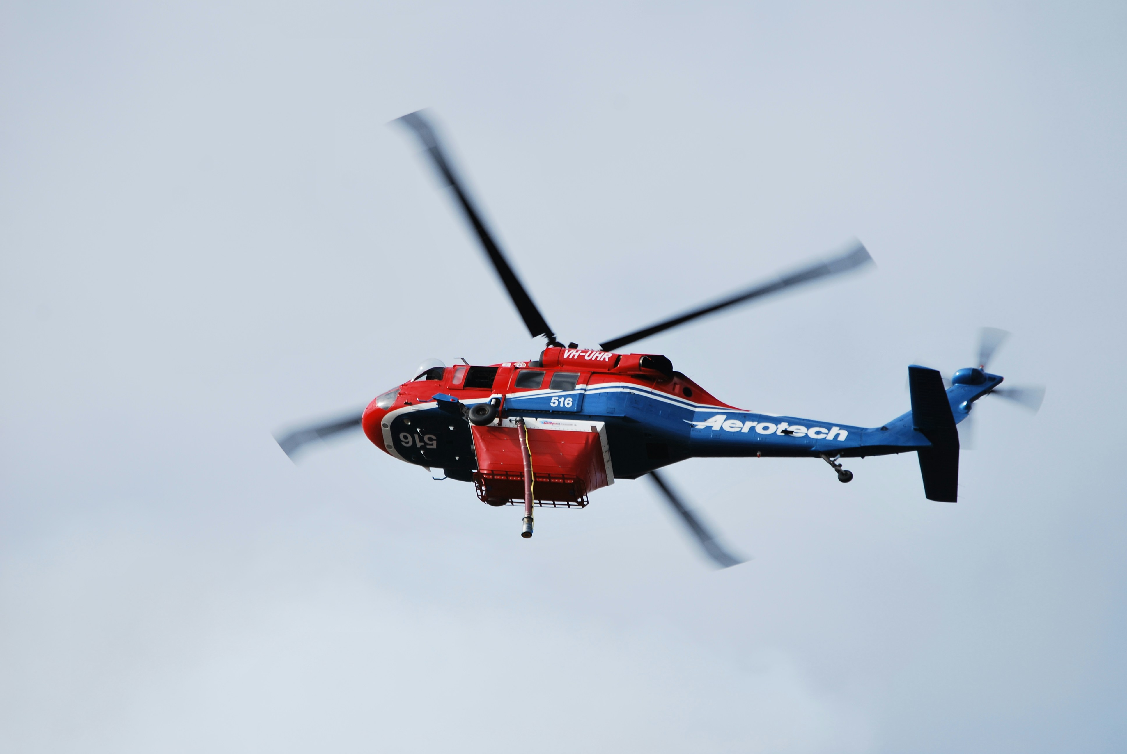 a red and blue helicopter flying through a cloudy sky