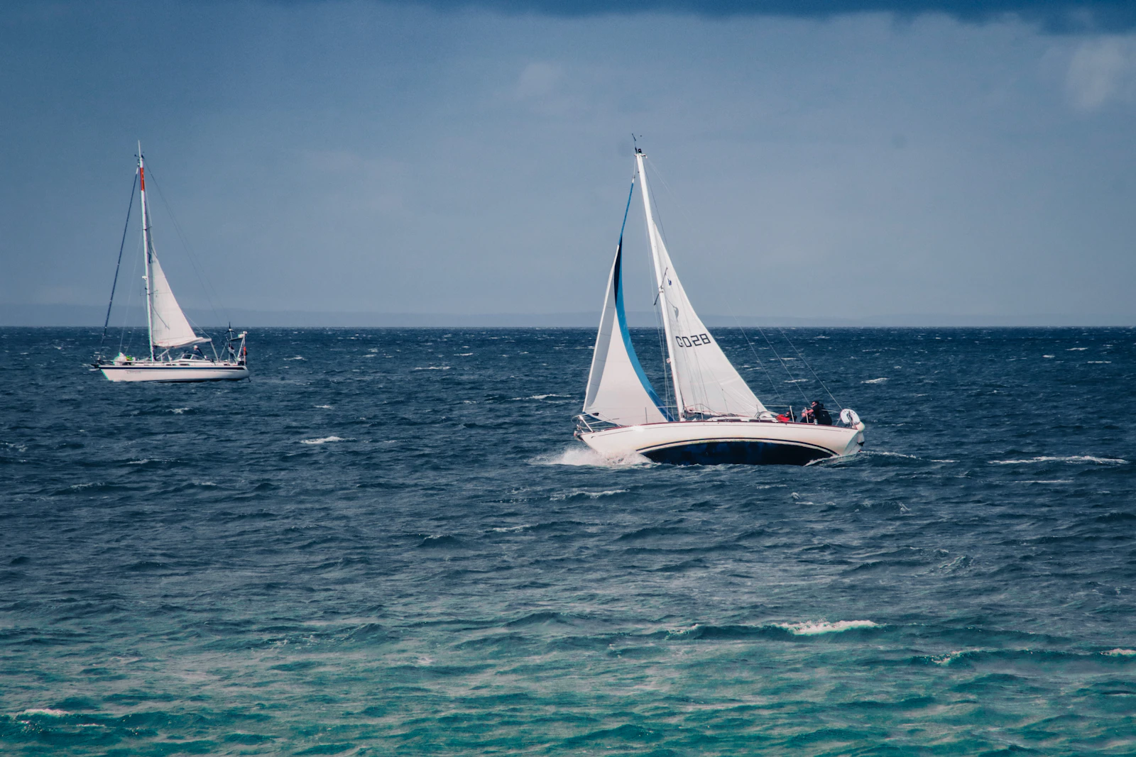 Two classic sailing yachts racing side by side on a sparkling sea