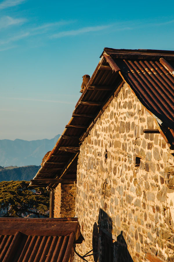 A stone house with a brown roof below a mountain