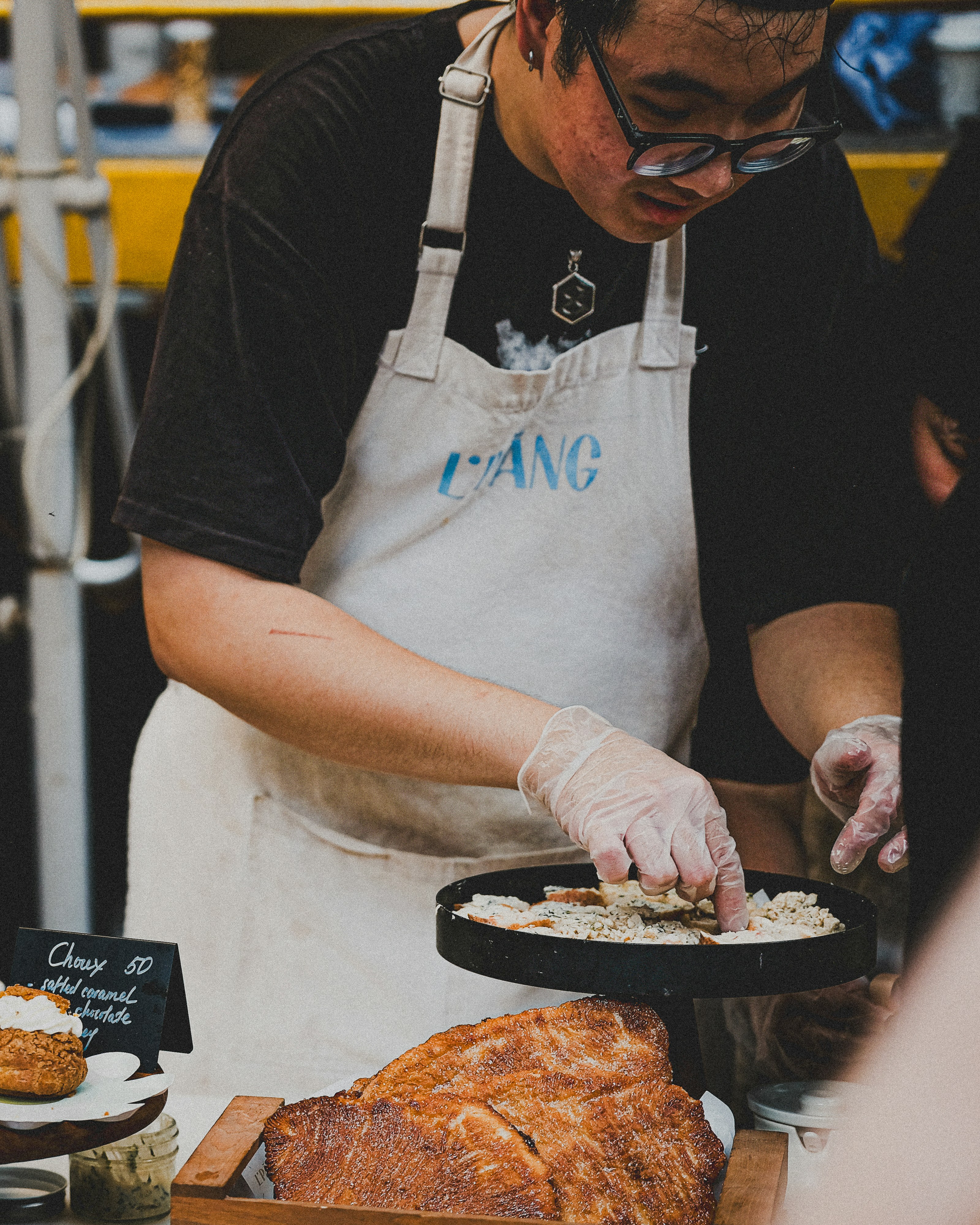 a man in an apron putting toppings on a loaf of bread