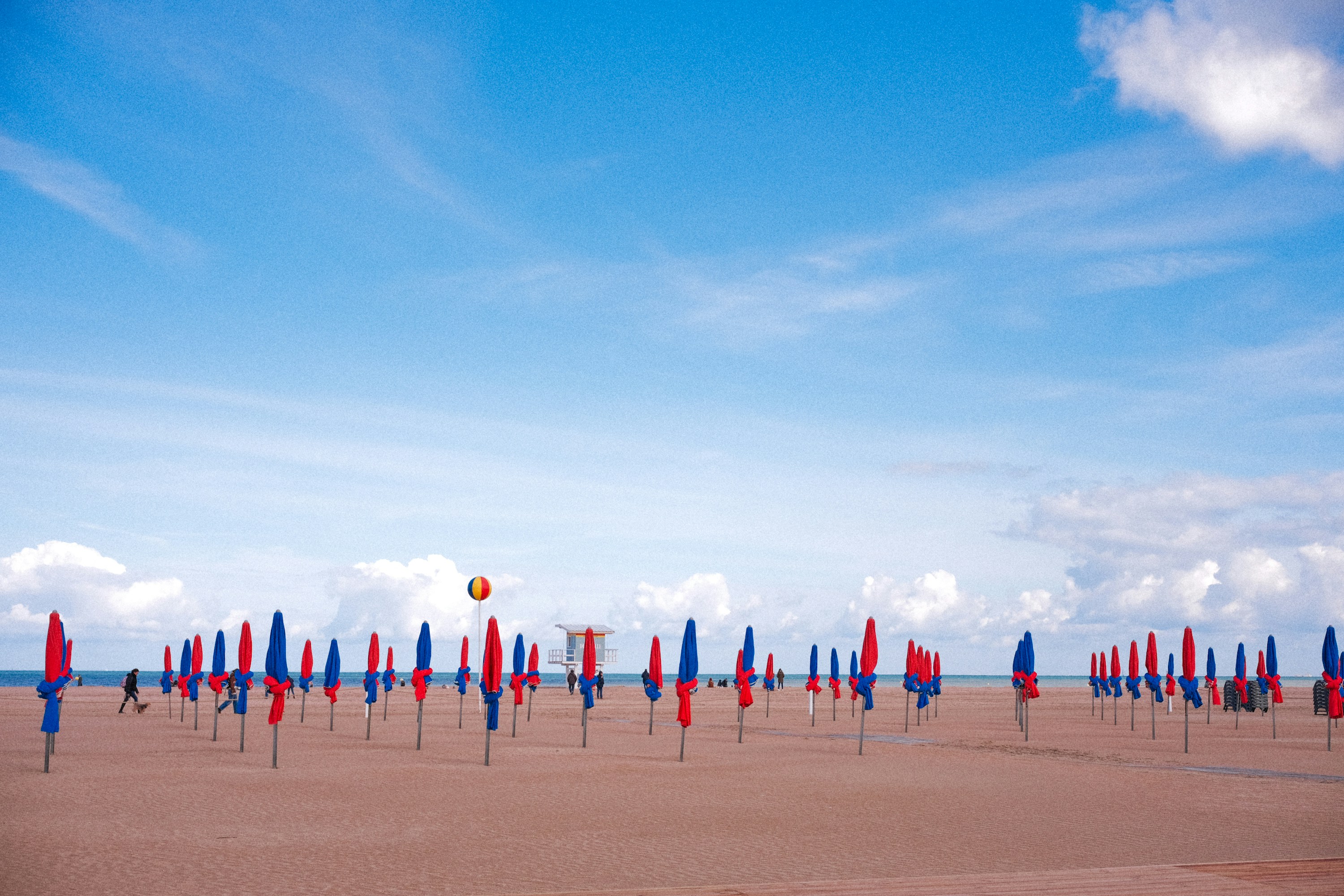 a beach filled with lots of blue and red umbrellas, 