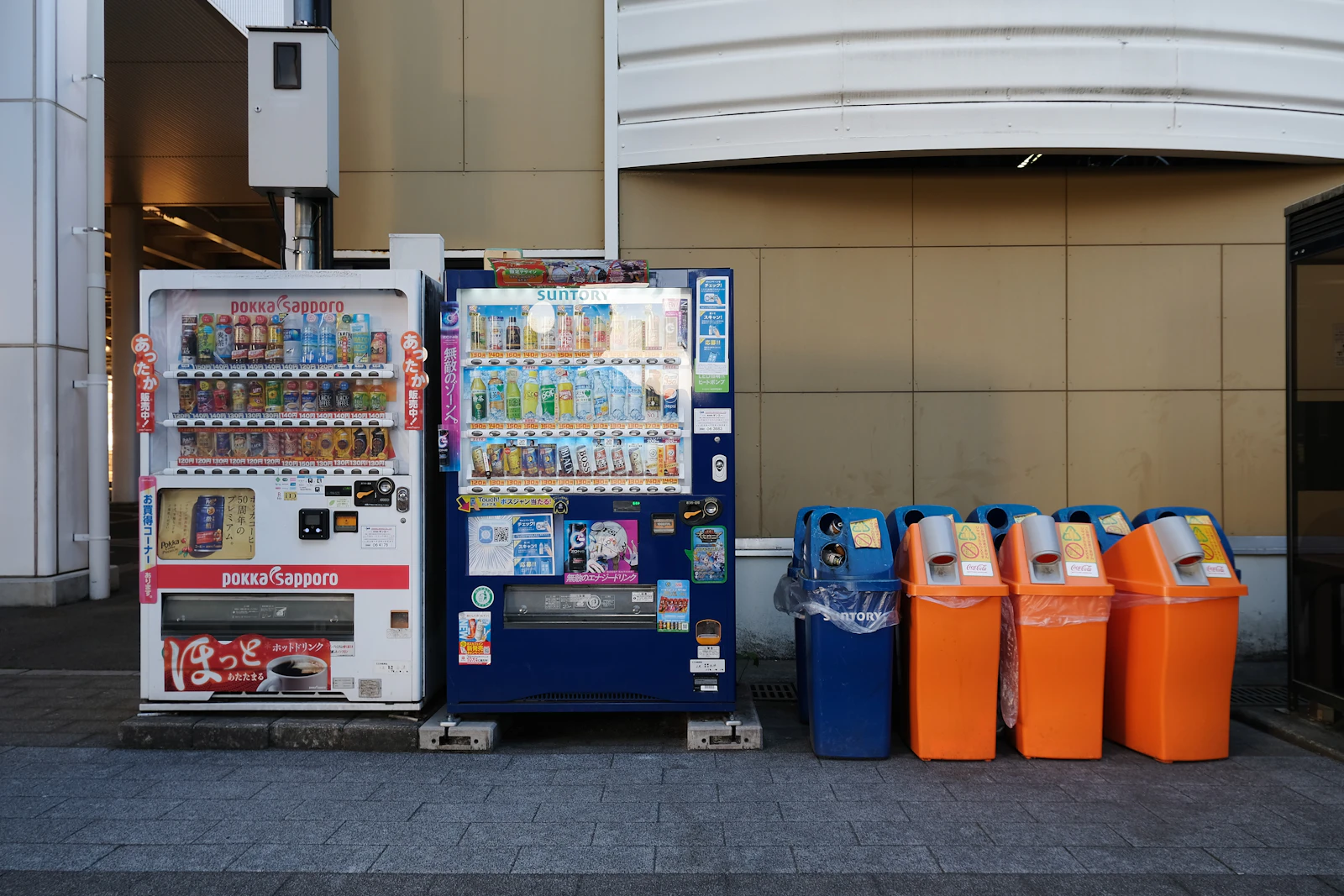 Drink vending machines beside marked bottle and can collection boxes in Japan