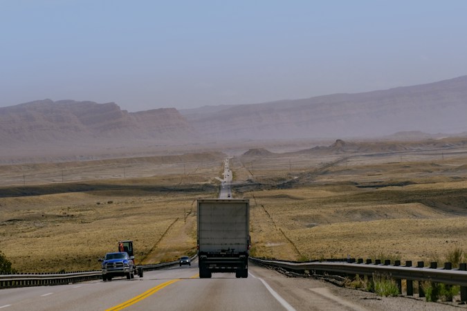 A semi truck drives down a desert highway, like the freight traffic moving along I-15 between Apex Industrial Park and the rest of the valley