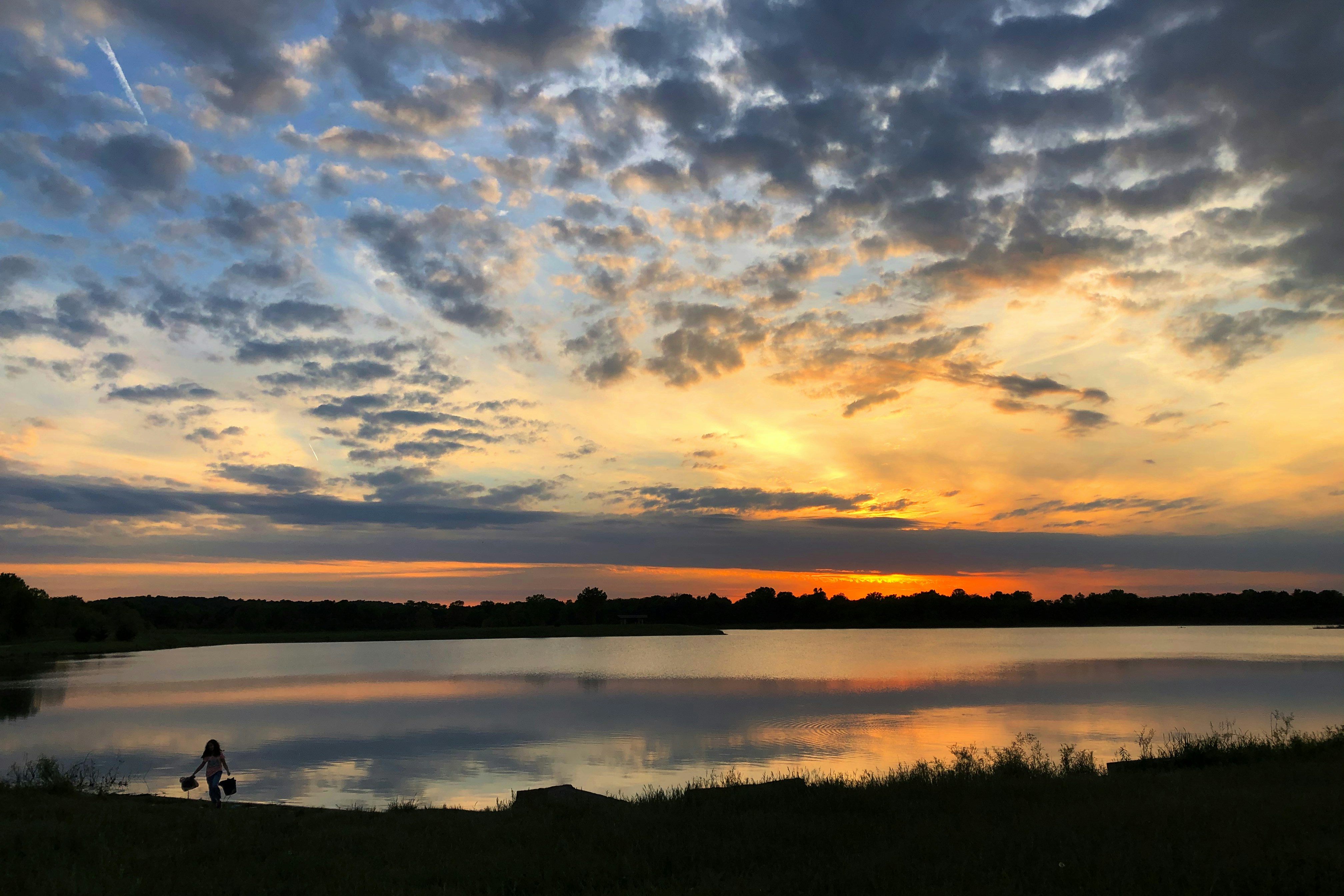 a person standing on the shore of a lake at sunset