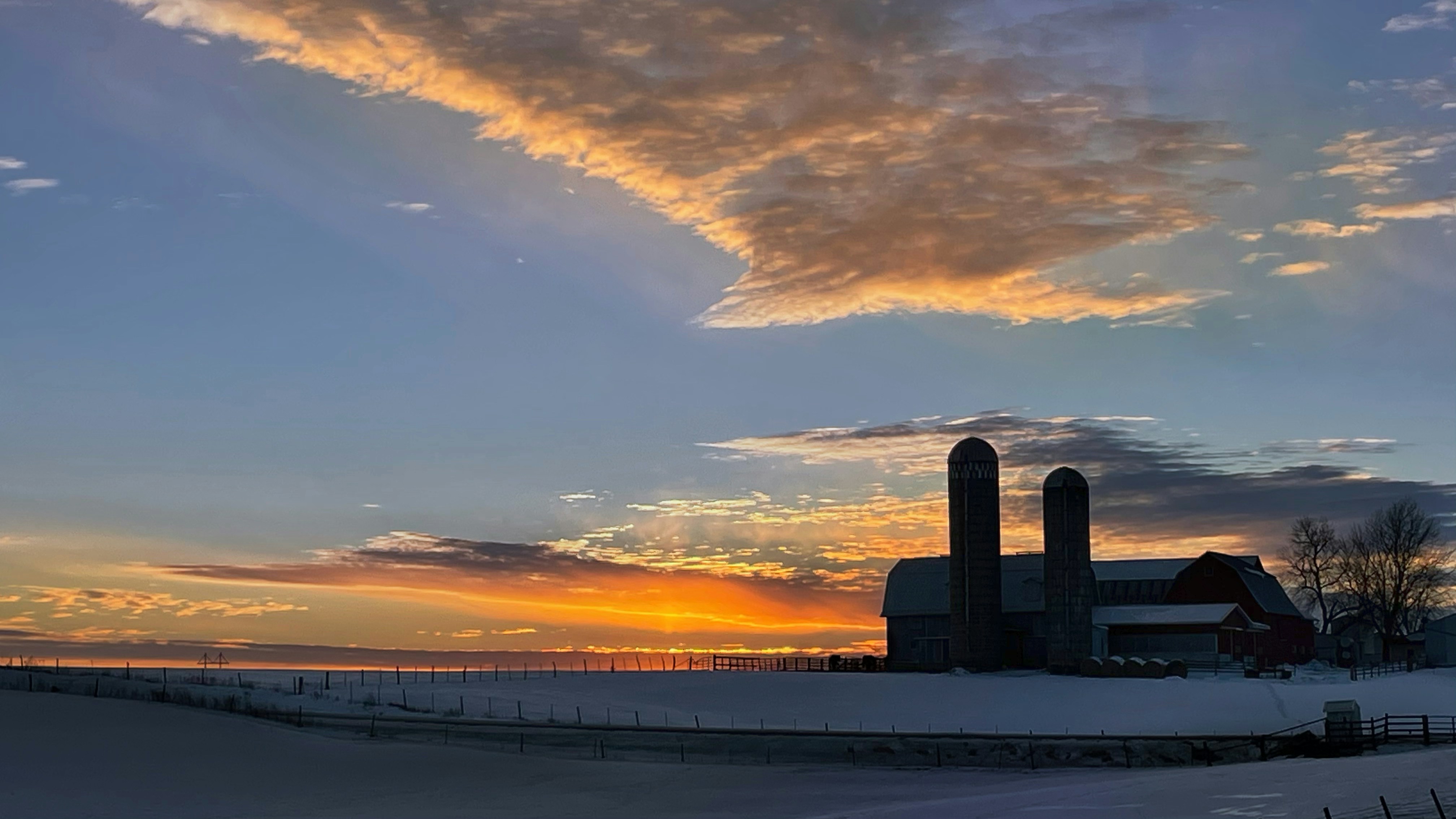 a barn in a snowy field with a sunset in the background