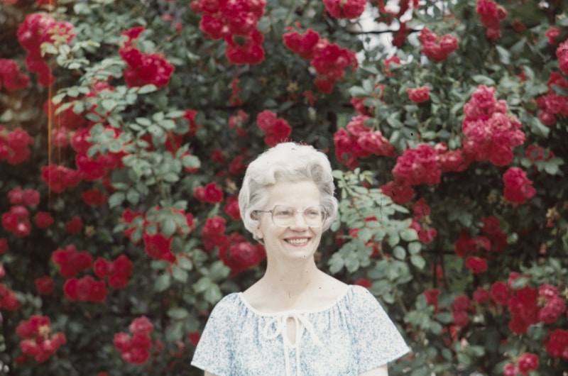 an old woman standing in front of a rose bush