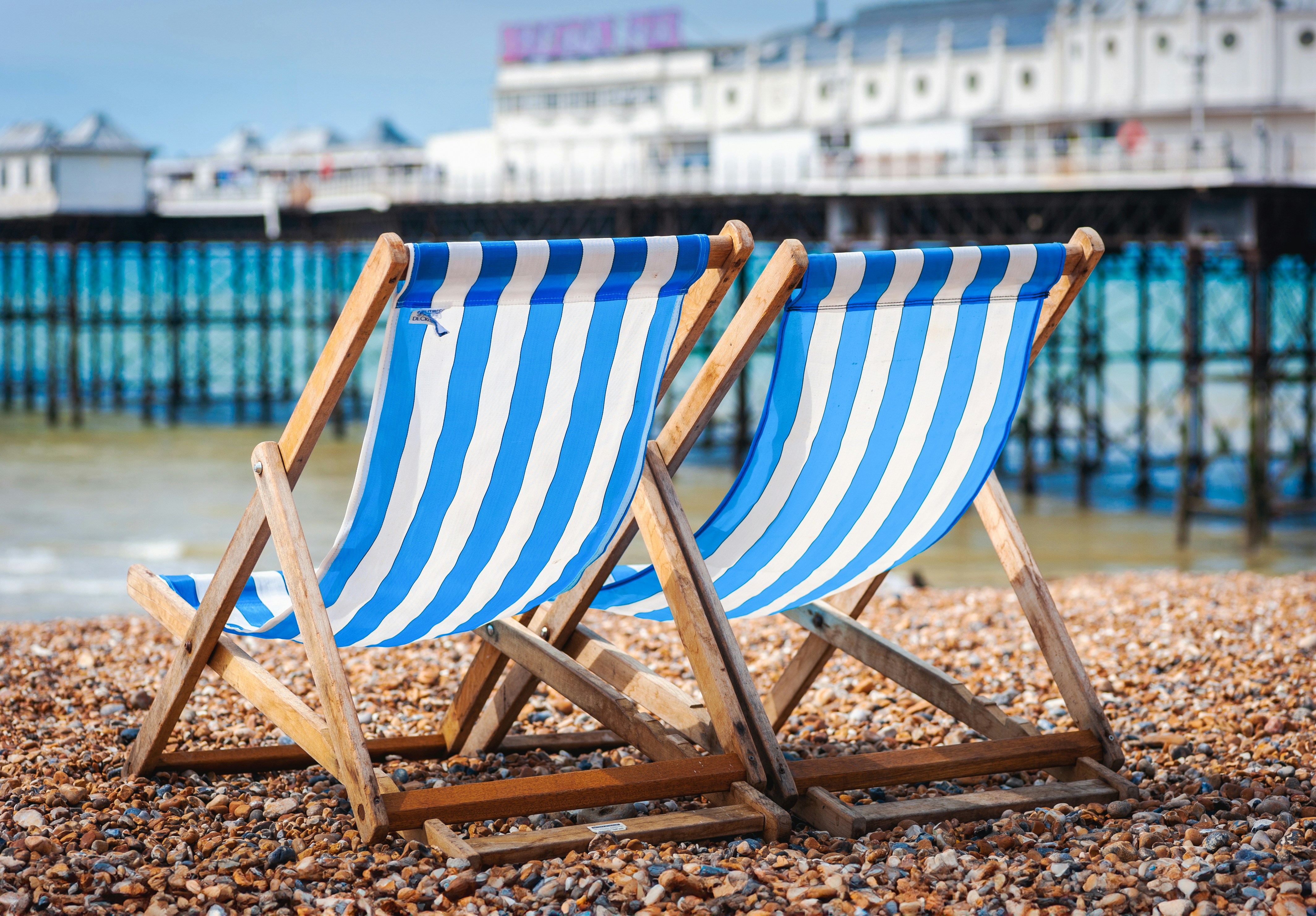 2 traditional striped deckchairs on a beach with a pier in the background
