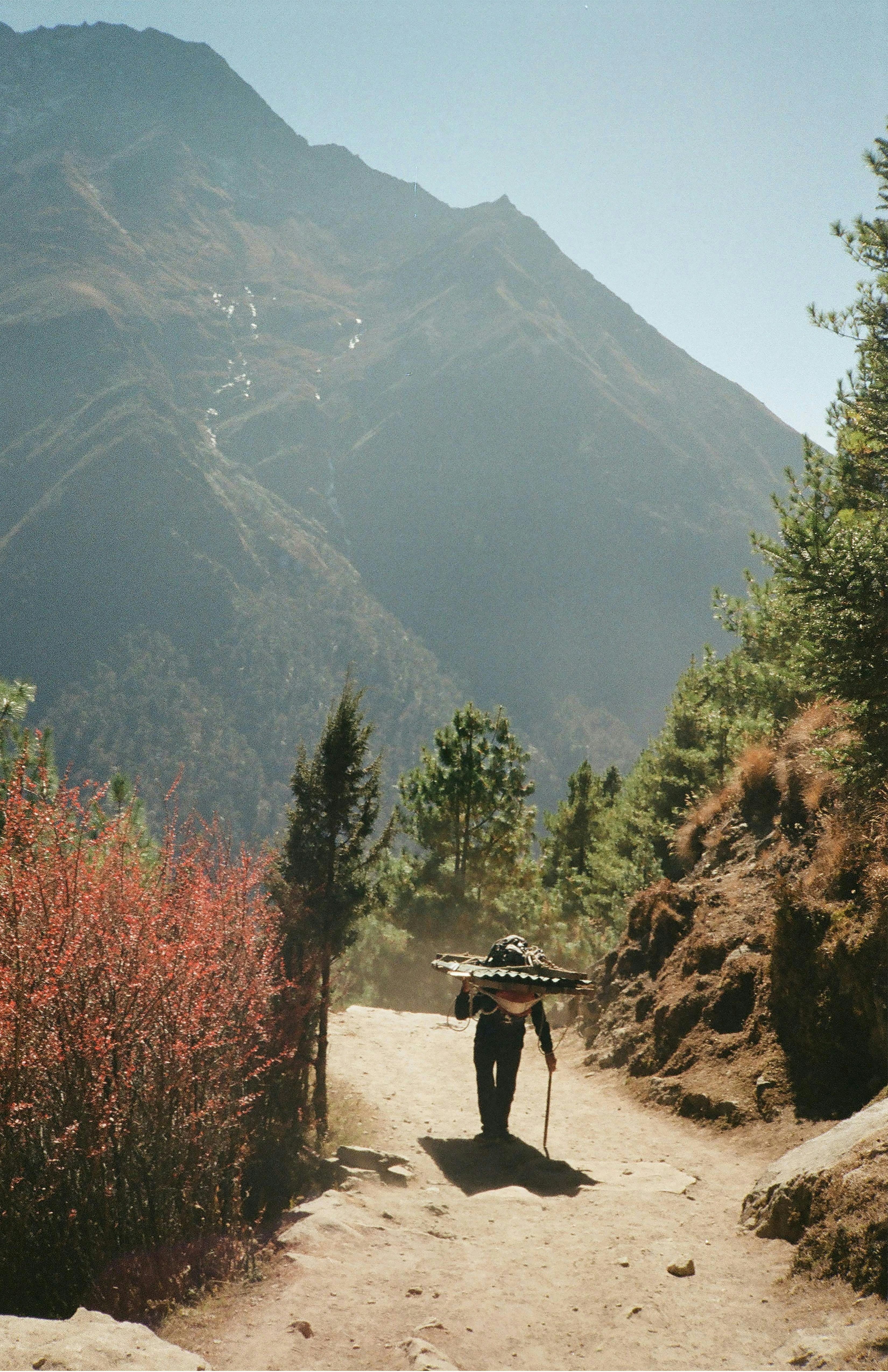 a man walking down a dirt road with a backpack on his head