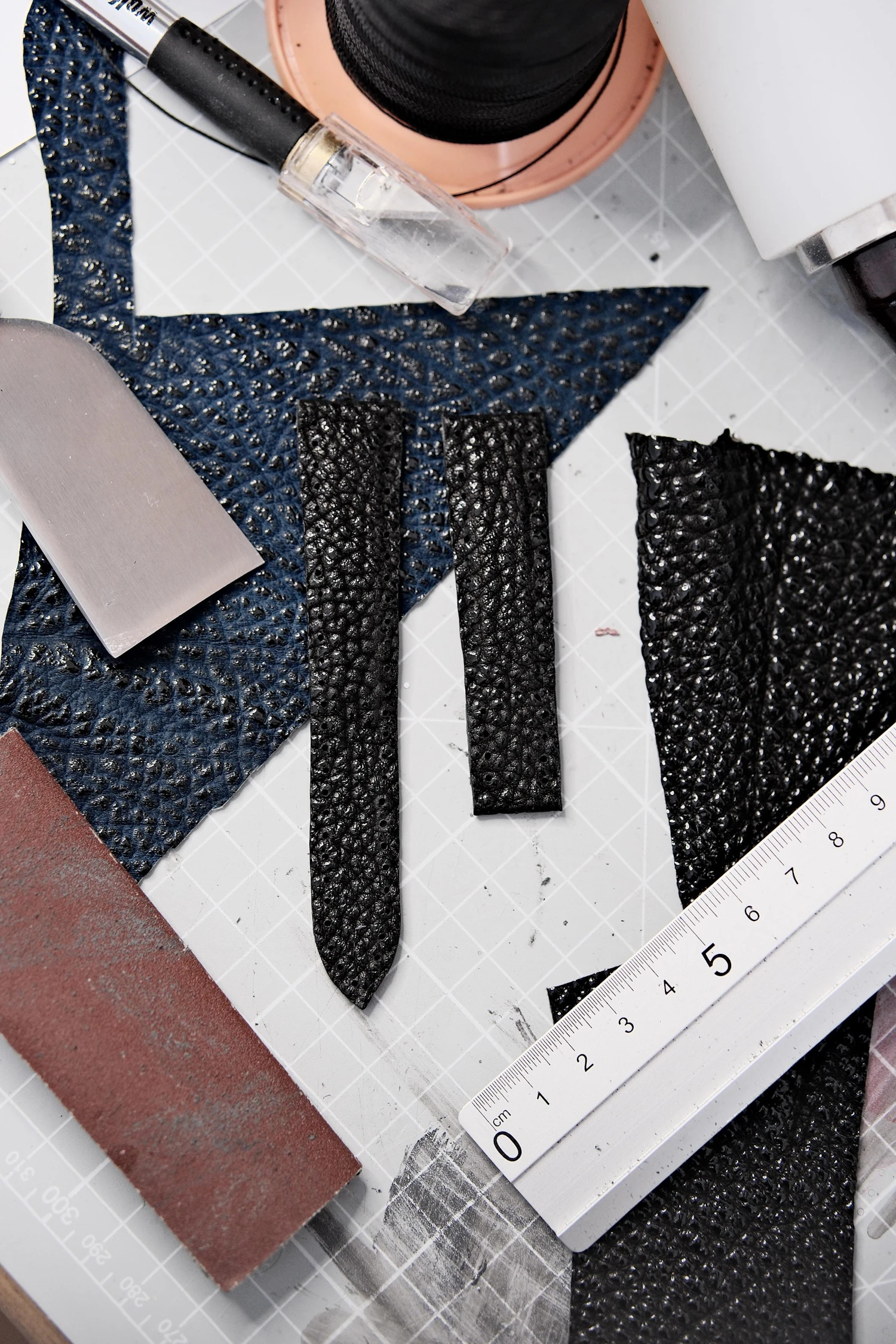 Leather strap blanks cut on a mat beside a steel rule and a skiving knife