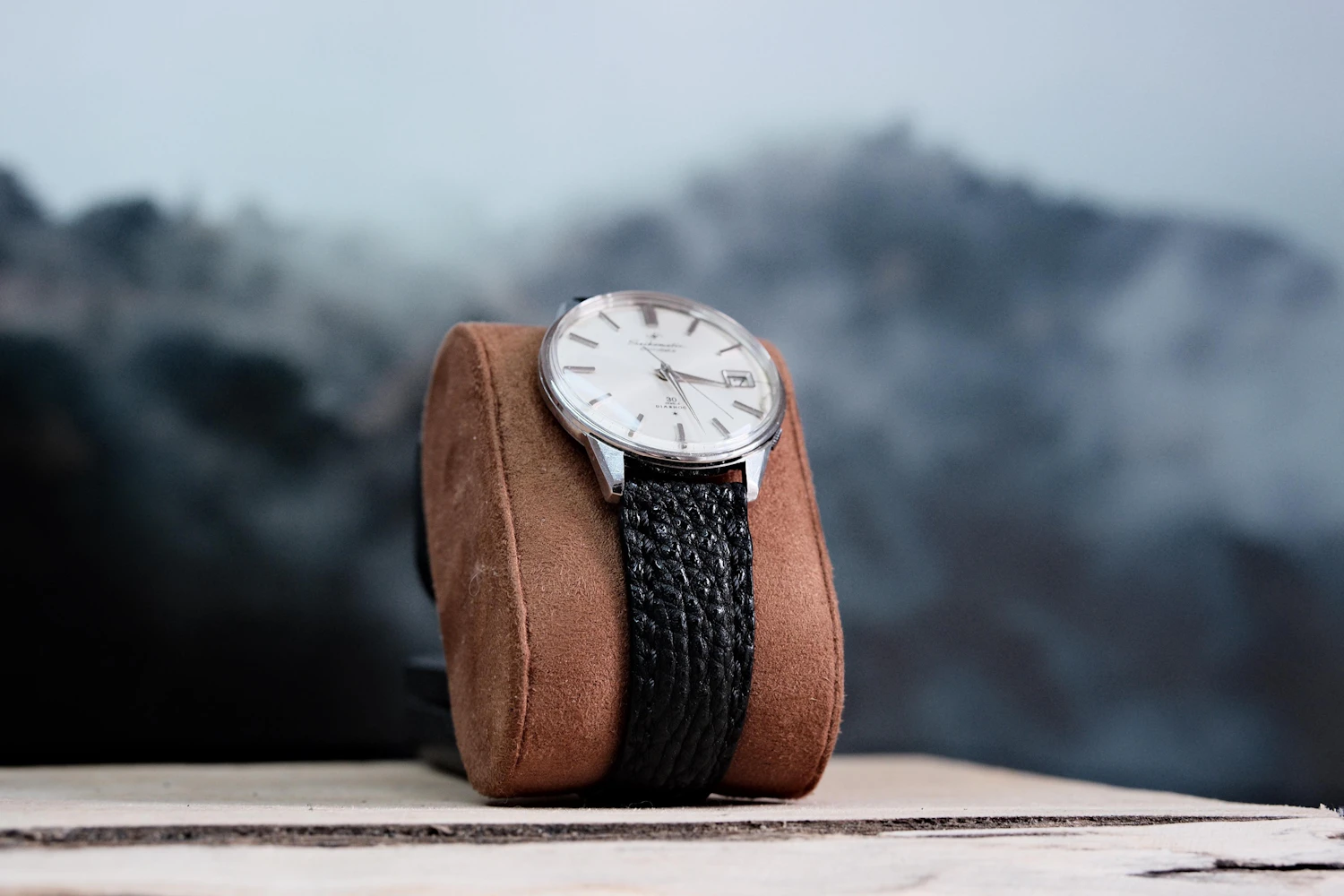 Brévine 38, a silver opaline dial on black calf wrapped round a suede pillow, misty hills behind — in stock