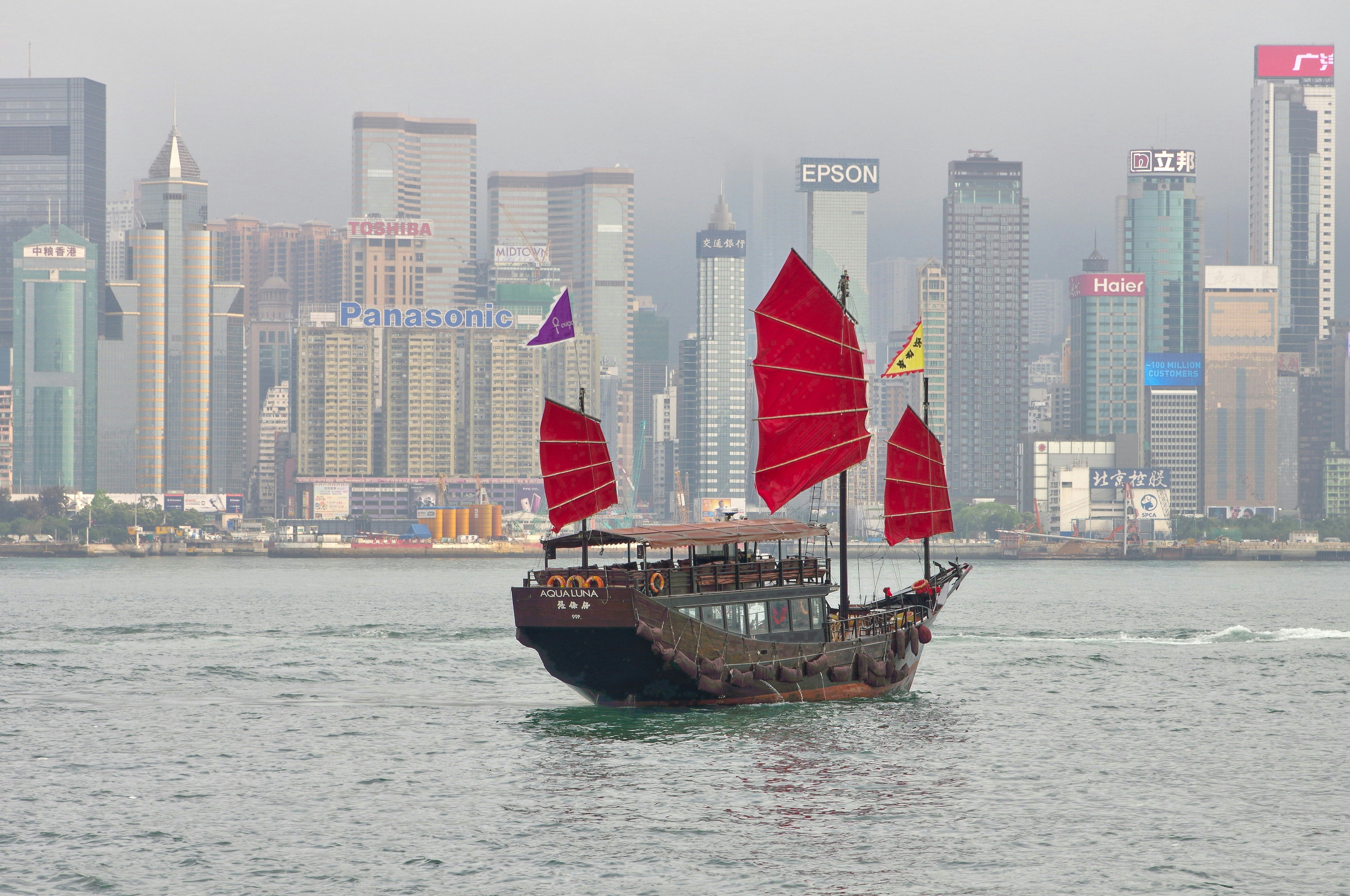 Ein Boot mit roten Segeln in einem Gewässer mit einer Stadt im Hintergrund