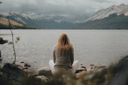 a woman sitting on a rock near a body of water