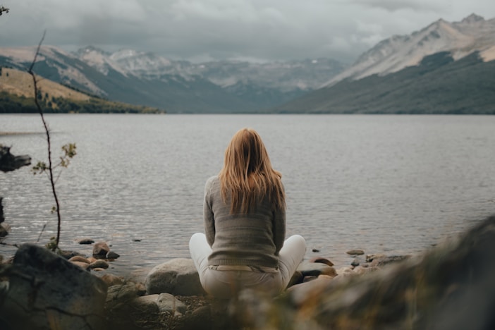 a woman sitting on a rock near a body of water