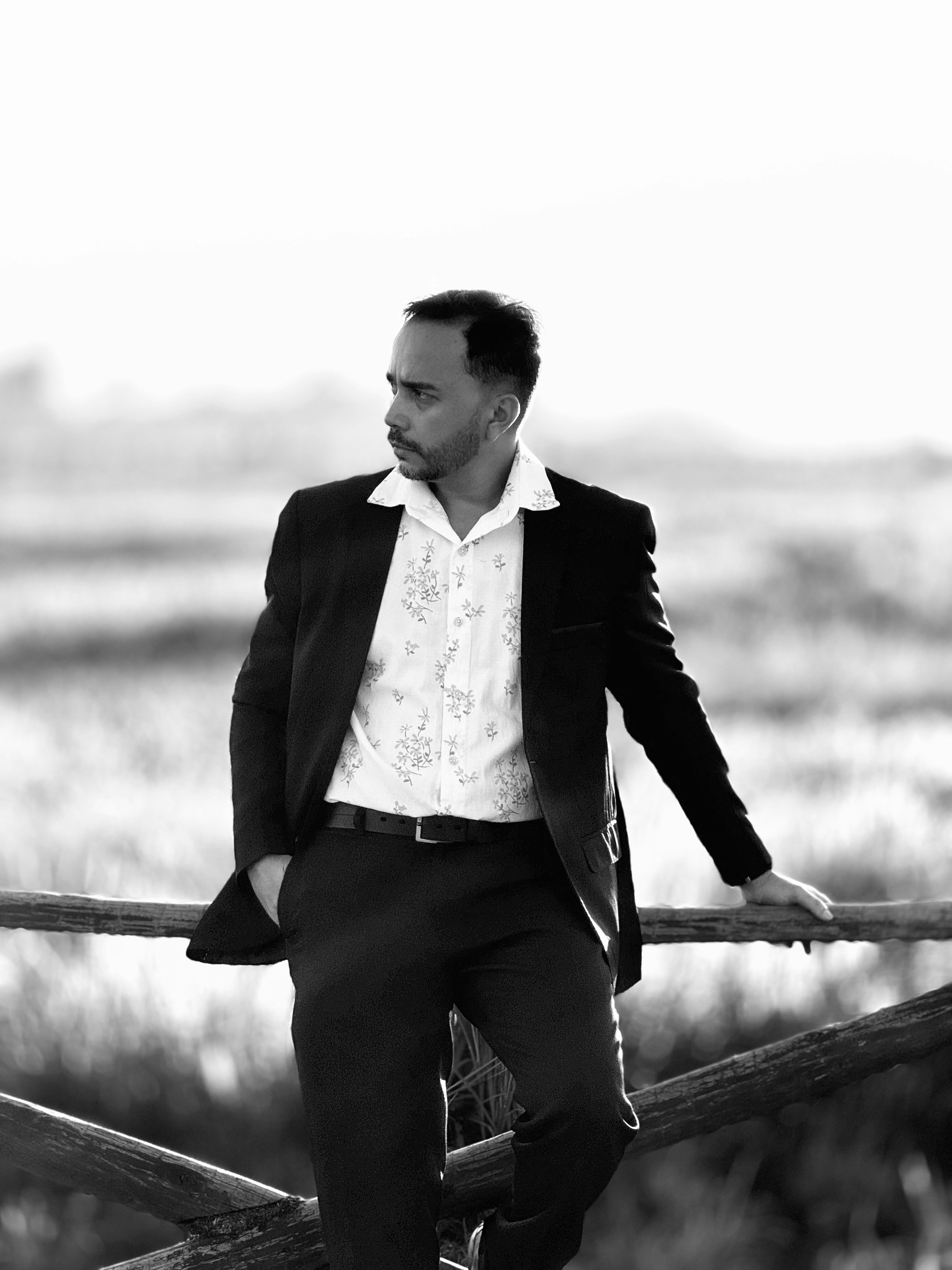 a man in a suit leaning on a fence