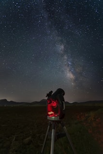 a telescope on a tripod in a field with the night sky in the background