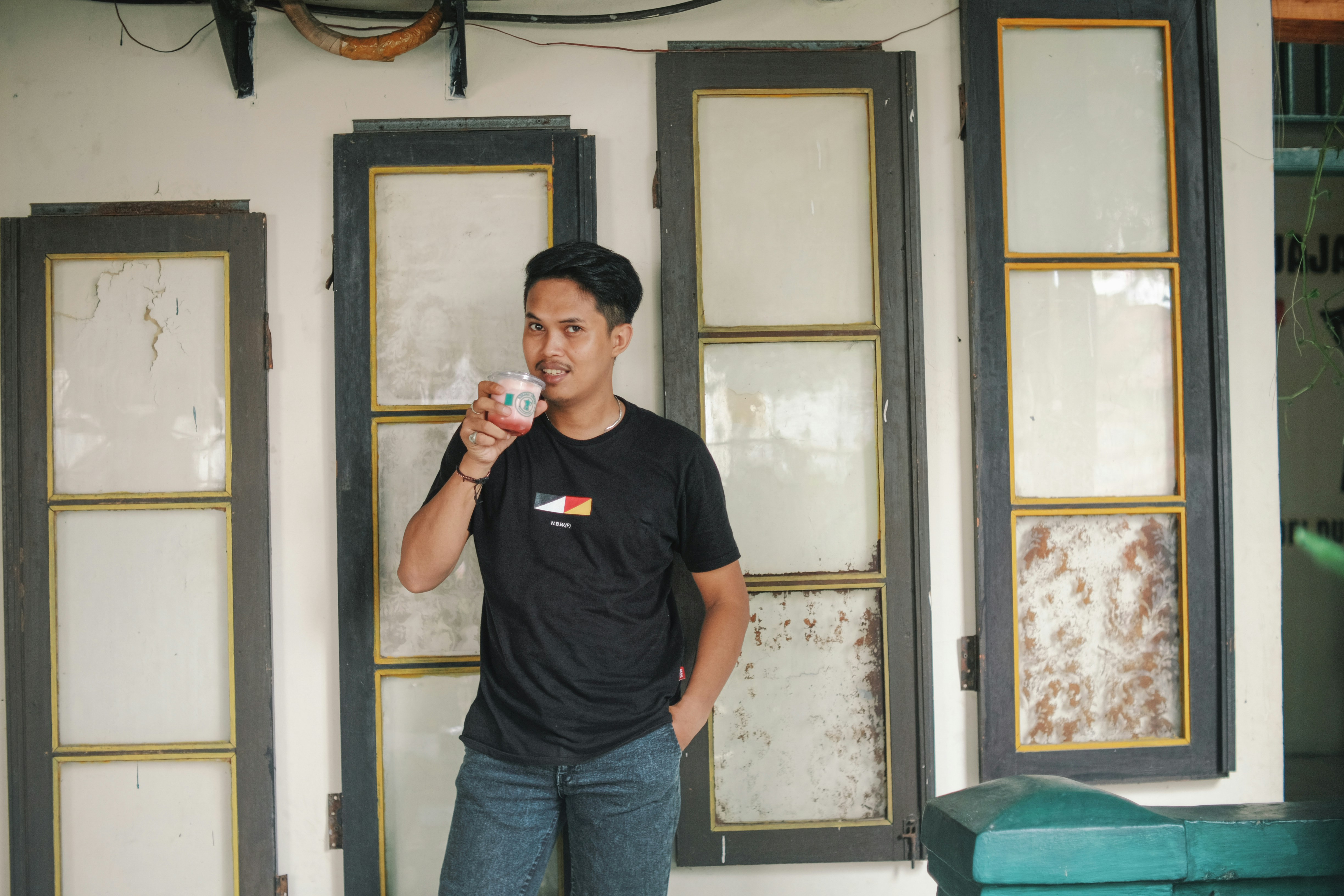 a man standing in front of a wall holding a drink