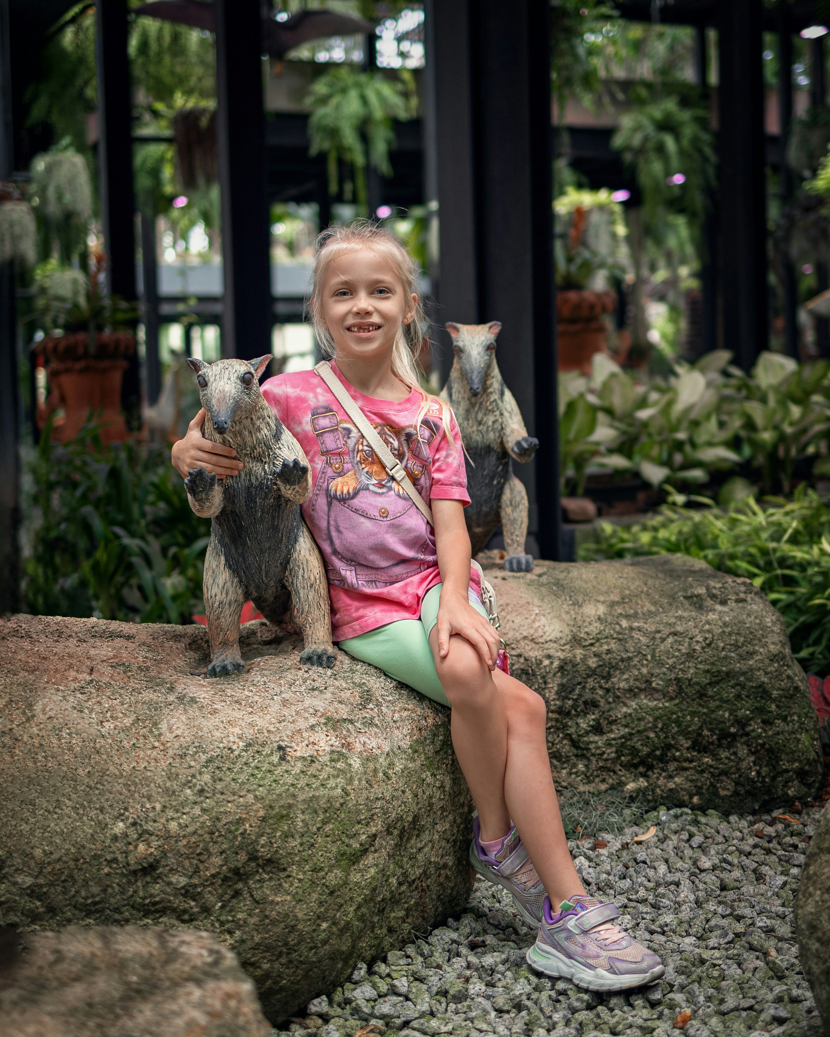 a little girl sitting on a rock with two stuffed animals