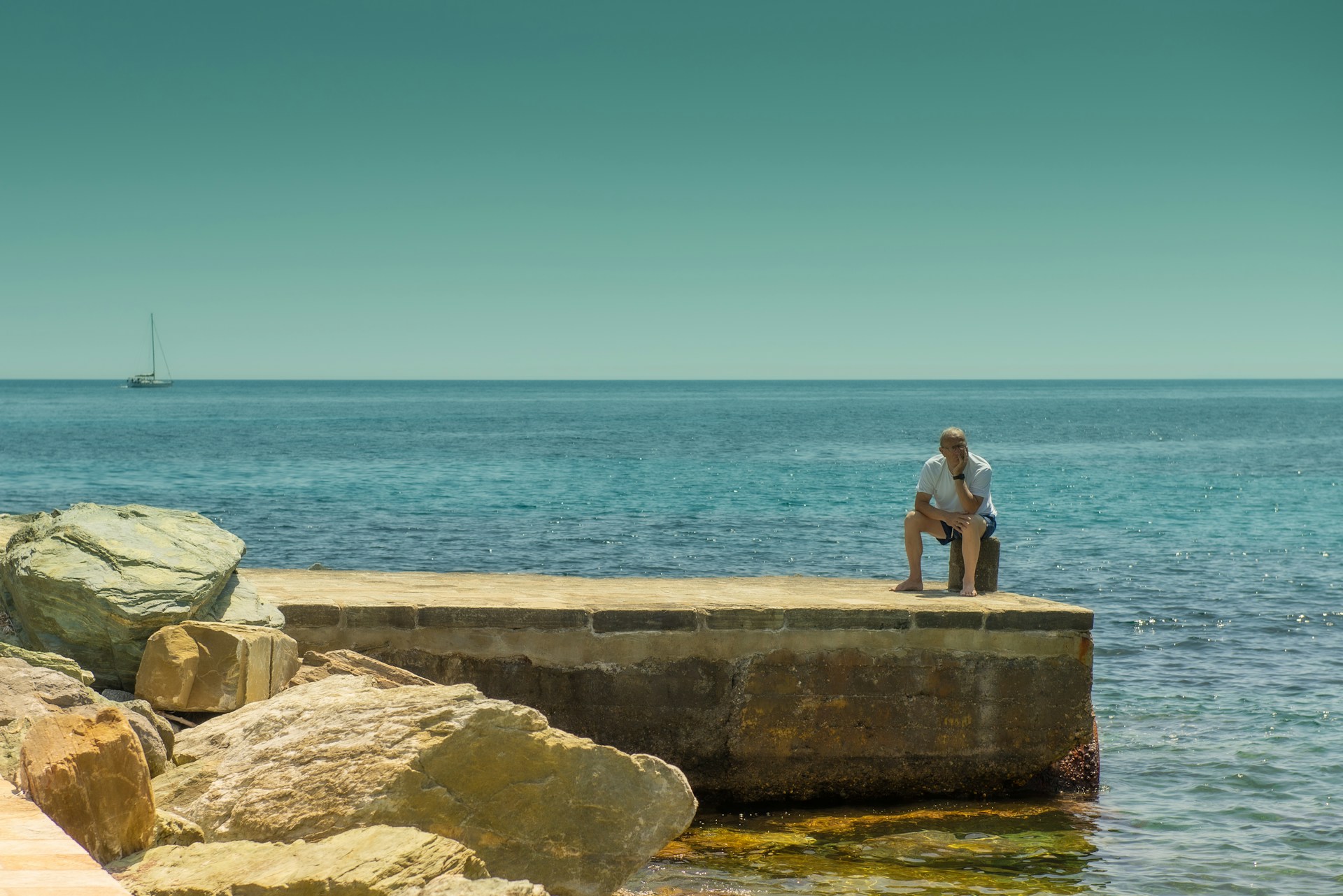 a man sitting on a rock next to a body of water