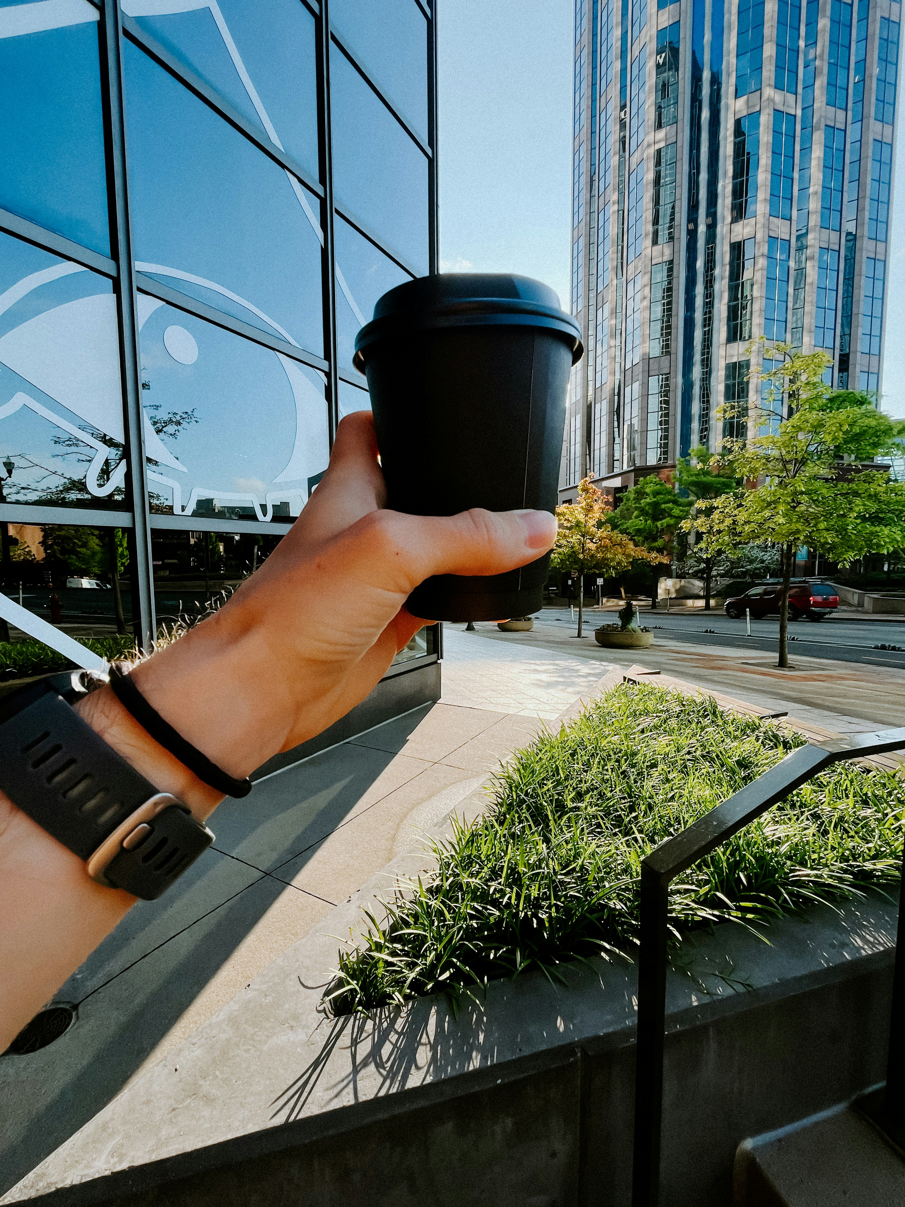 Рука держит стакан кофе на вынос, прогулка по городской улице