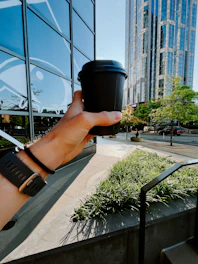 a hand holding a coffee cup in front of a building