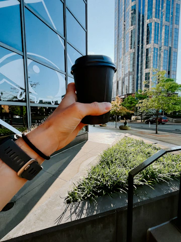 a hand holding a coffee cup in front of a building