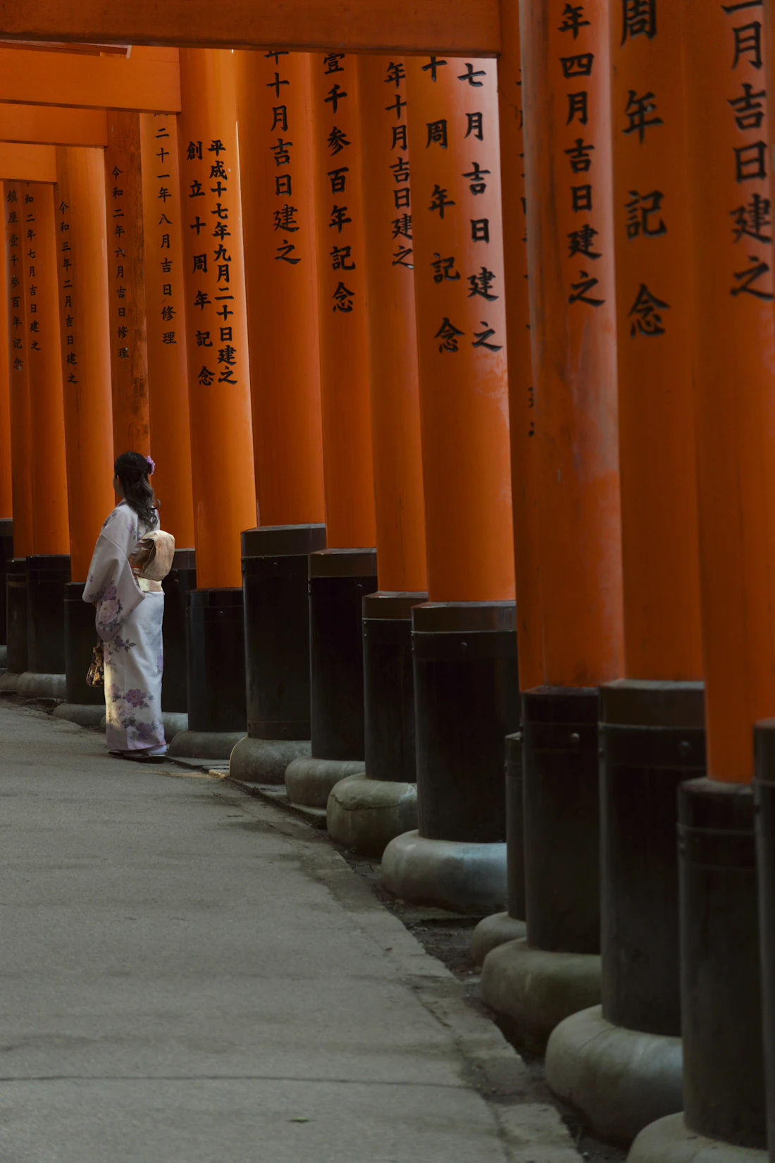 A woman in a white kimono standing before vermilion torii gates in Kyoto, Japan