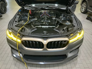 a silver car with its hood open and a yellow wire connected to it