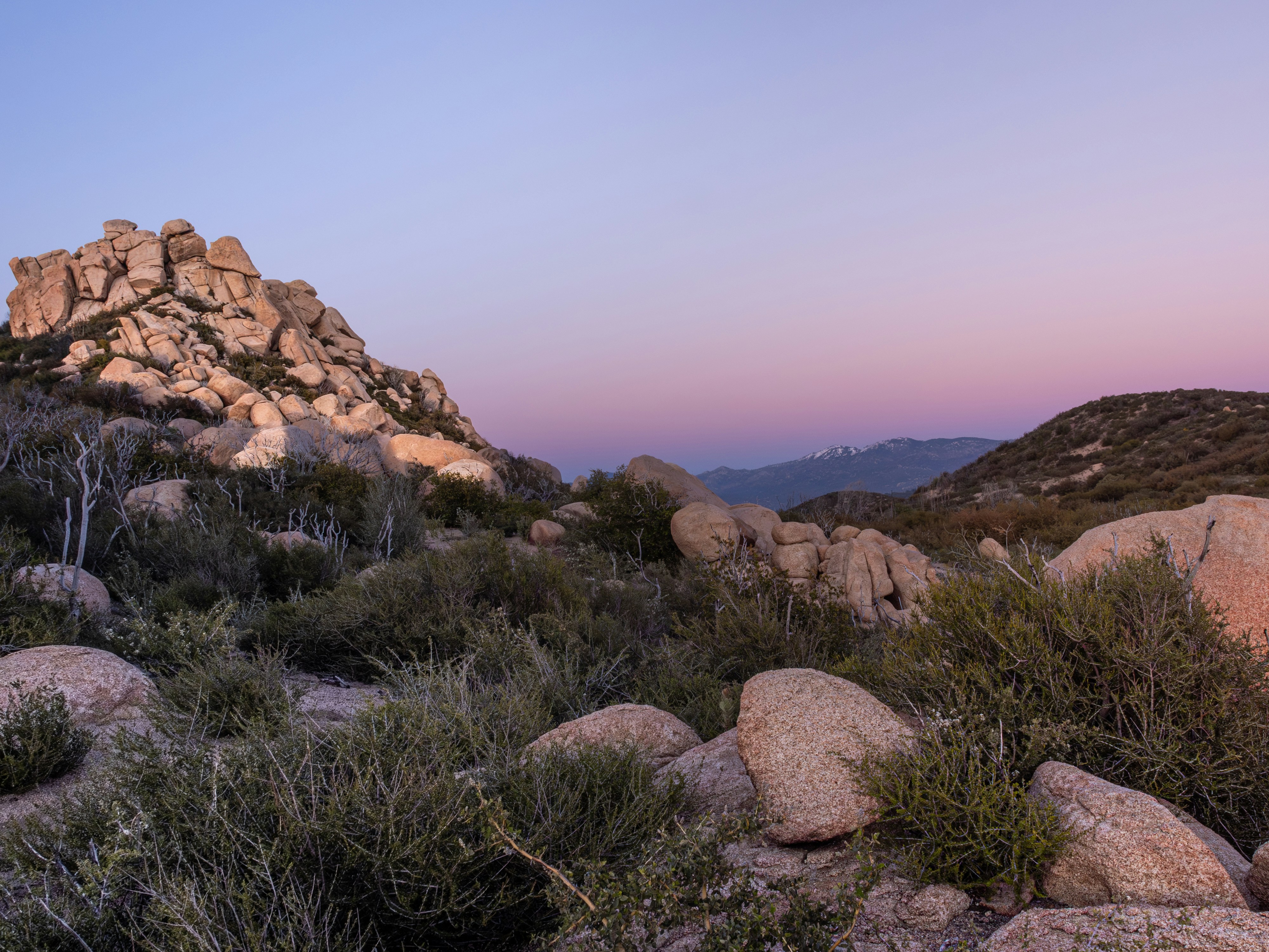 a rocky mountain with a pink sky in the background, Sunset. Mojave Desert, California.