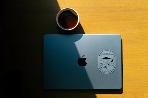A laptop on a wooden table next to a cup of coffee