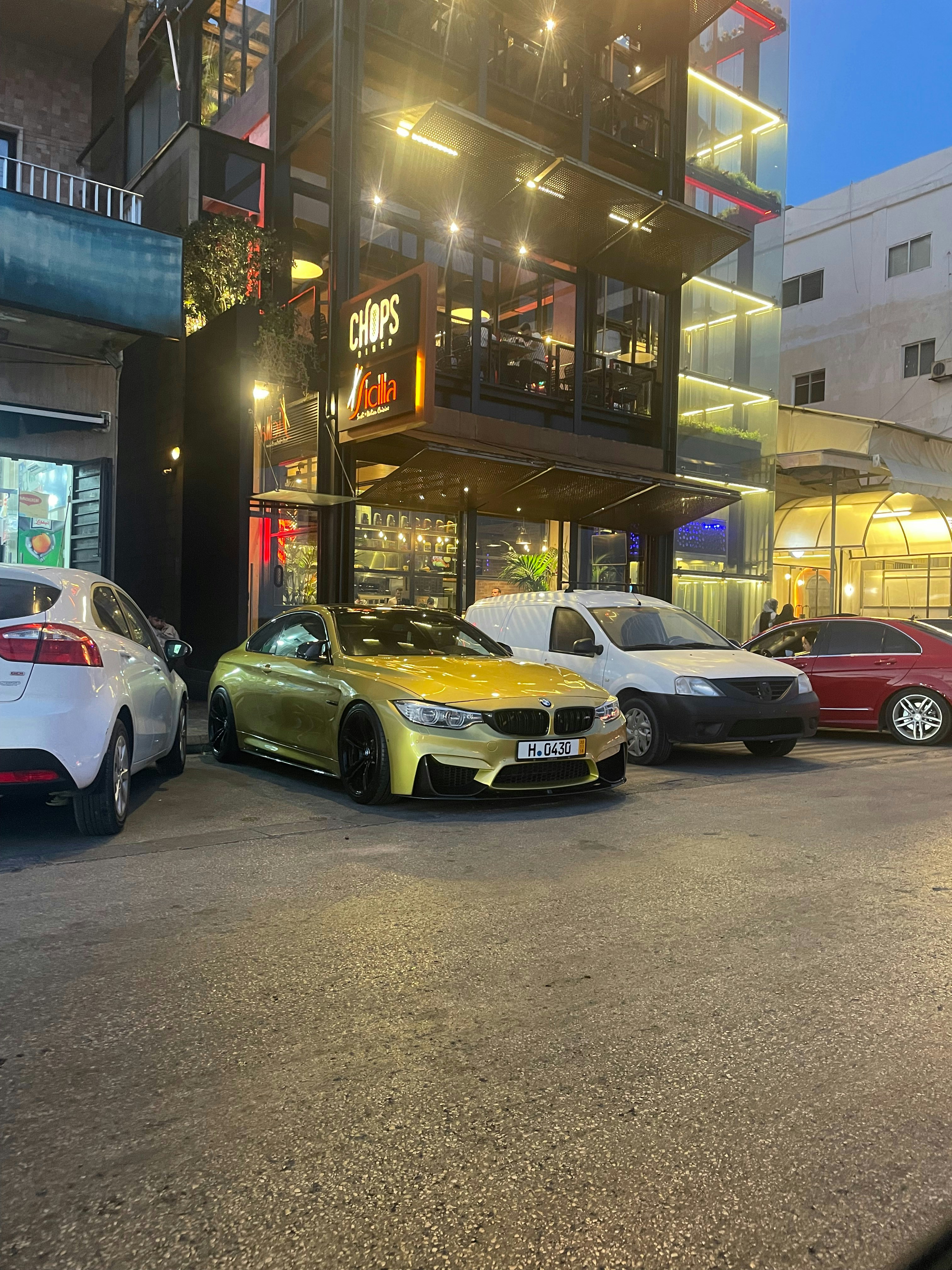 BMW M4 Competition parked in modern urban setting at twilight with city lights reflecting on bodywork