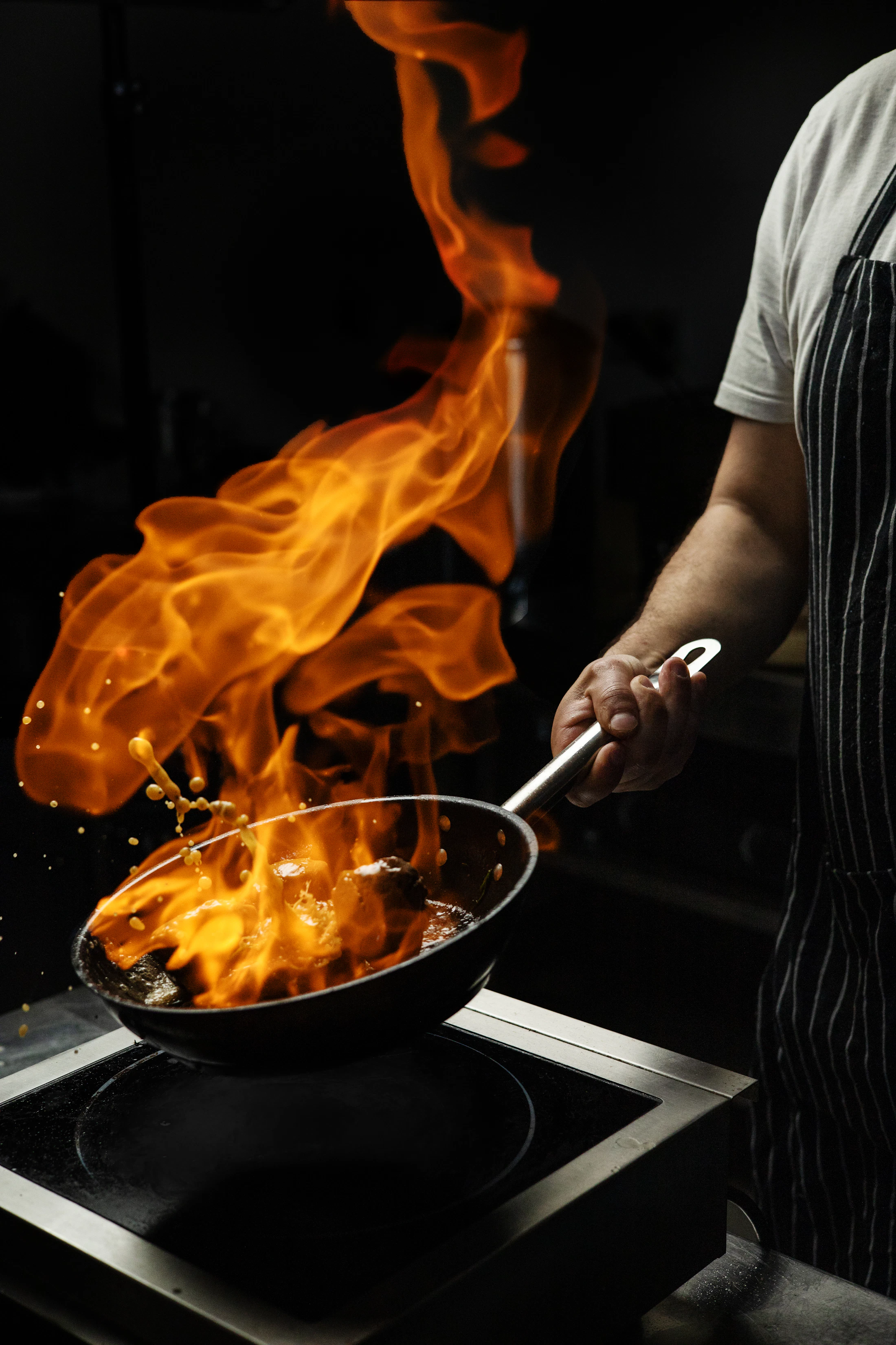 A chef throwing a pan of flame in a blacked-out kitchen