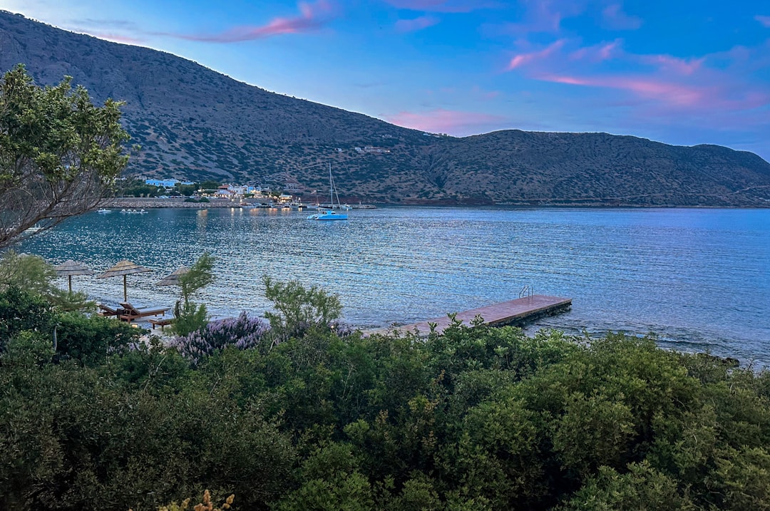 a body of water surrounded by trees and mountains, This great view is from blue door tavern just opposite Spinalonga viewing Plaka beach