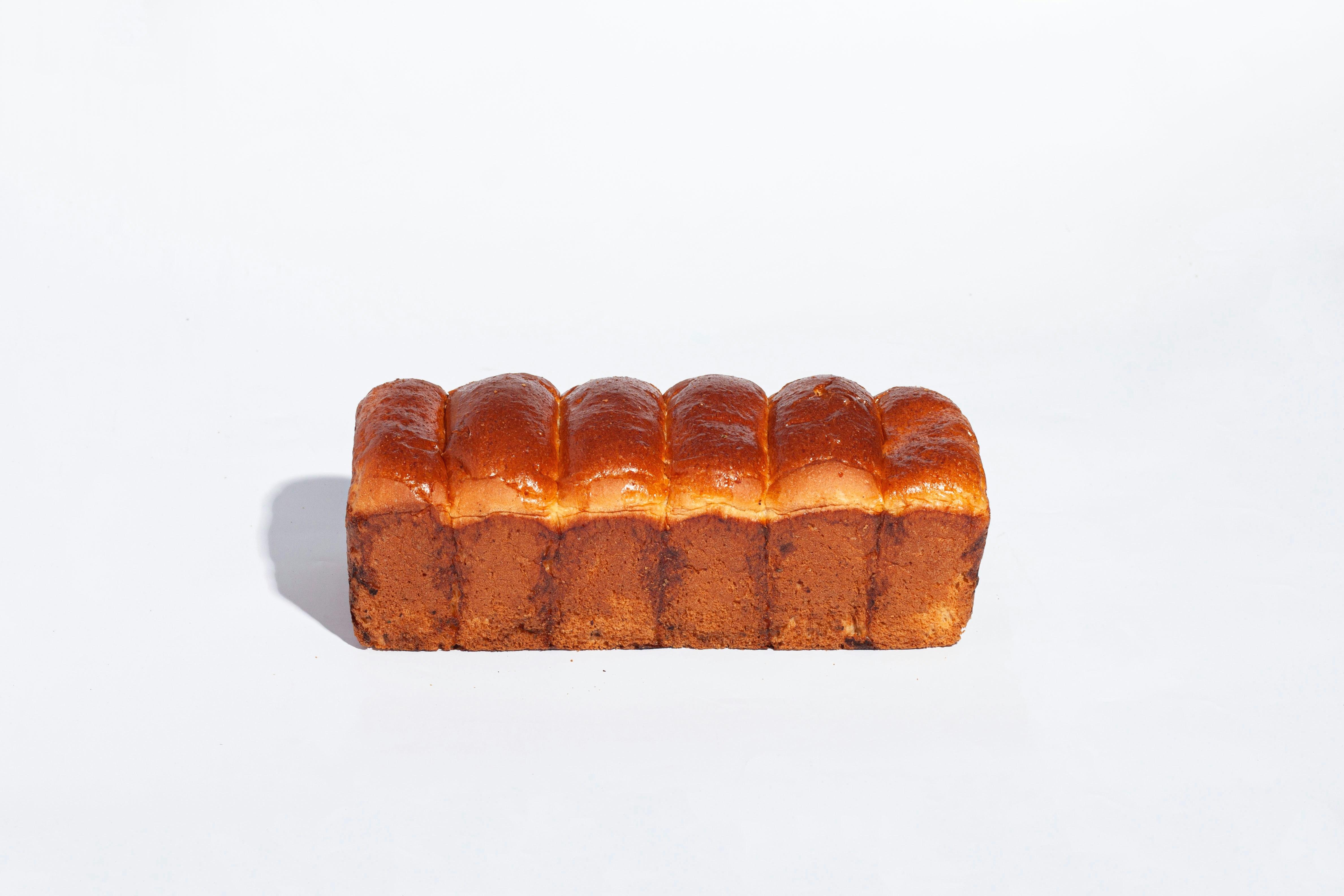 Shiny golden brioche loaf sliced on white surface, soft pillowy interior, warm studio light